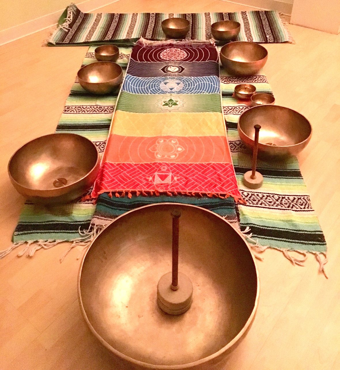 Healing bowls on yoga blankets with a colorful chakra blanket on top.